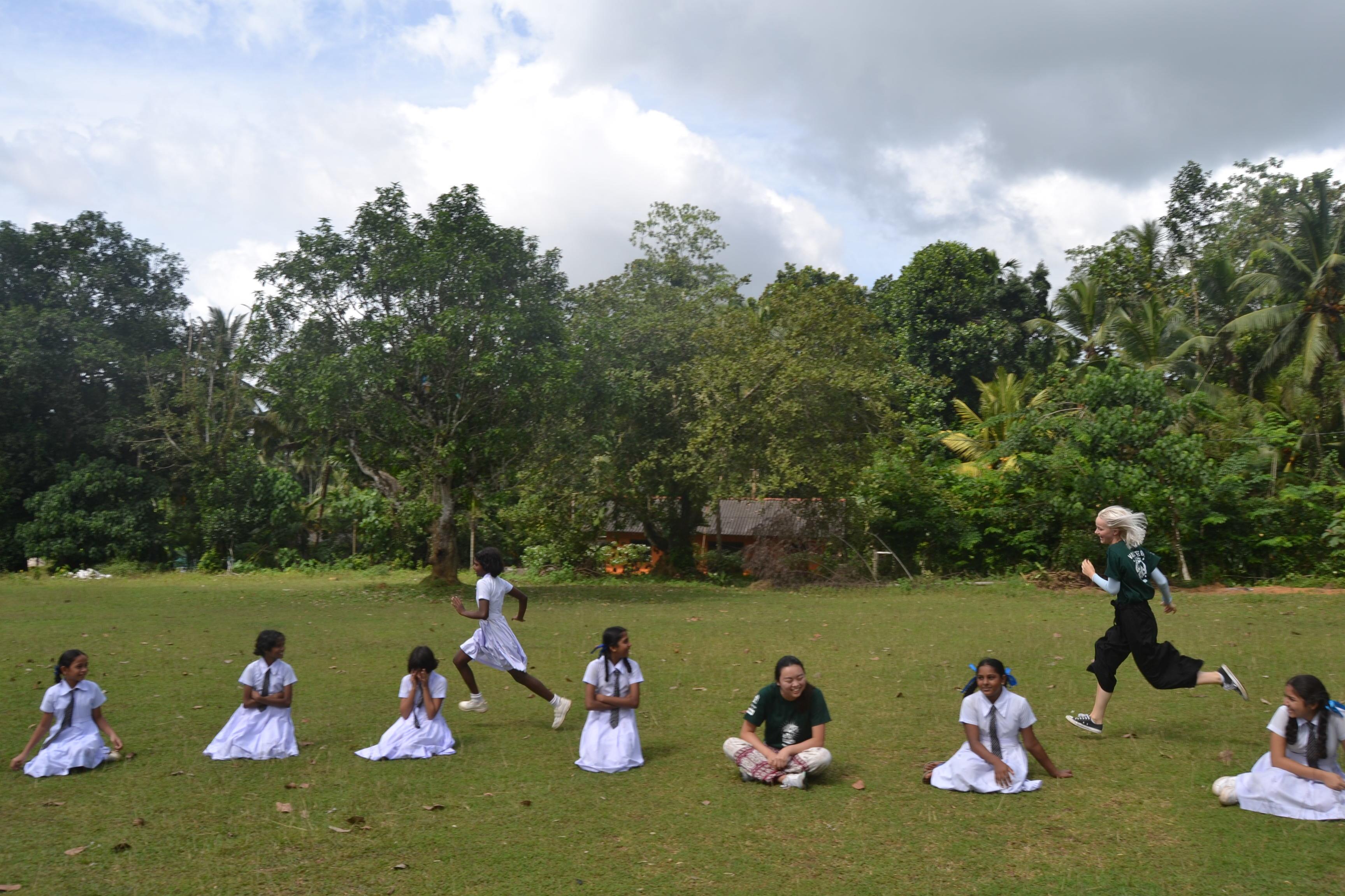 A Projects Abroad volunteer doing childcare work in Sri Lanka with a group, plays a game outside with the children. A volunteer doing community work in Sri Lanka with a group, runs outside with children during a game.